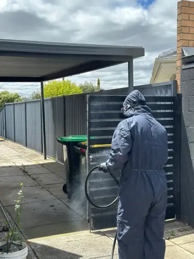 Licensed technician spray-treating a residential fence and bin area